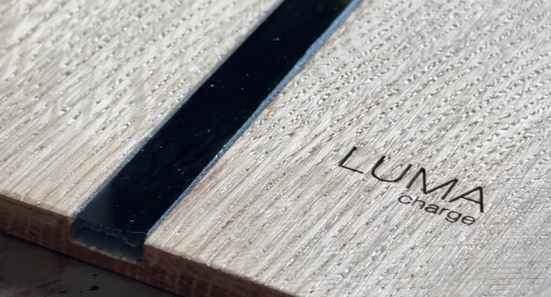 Zbliżenie na ręcznie wykonaną inkrustację i grawerowane logo LUMA charge na froncie z naturalnego drewna
